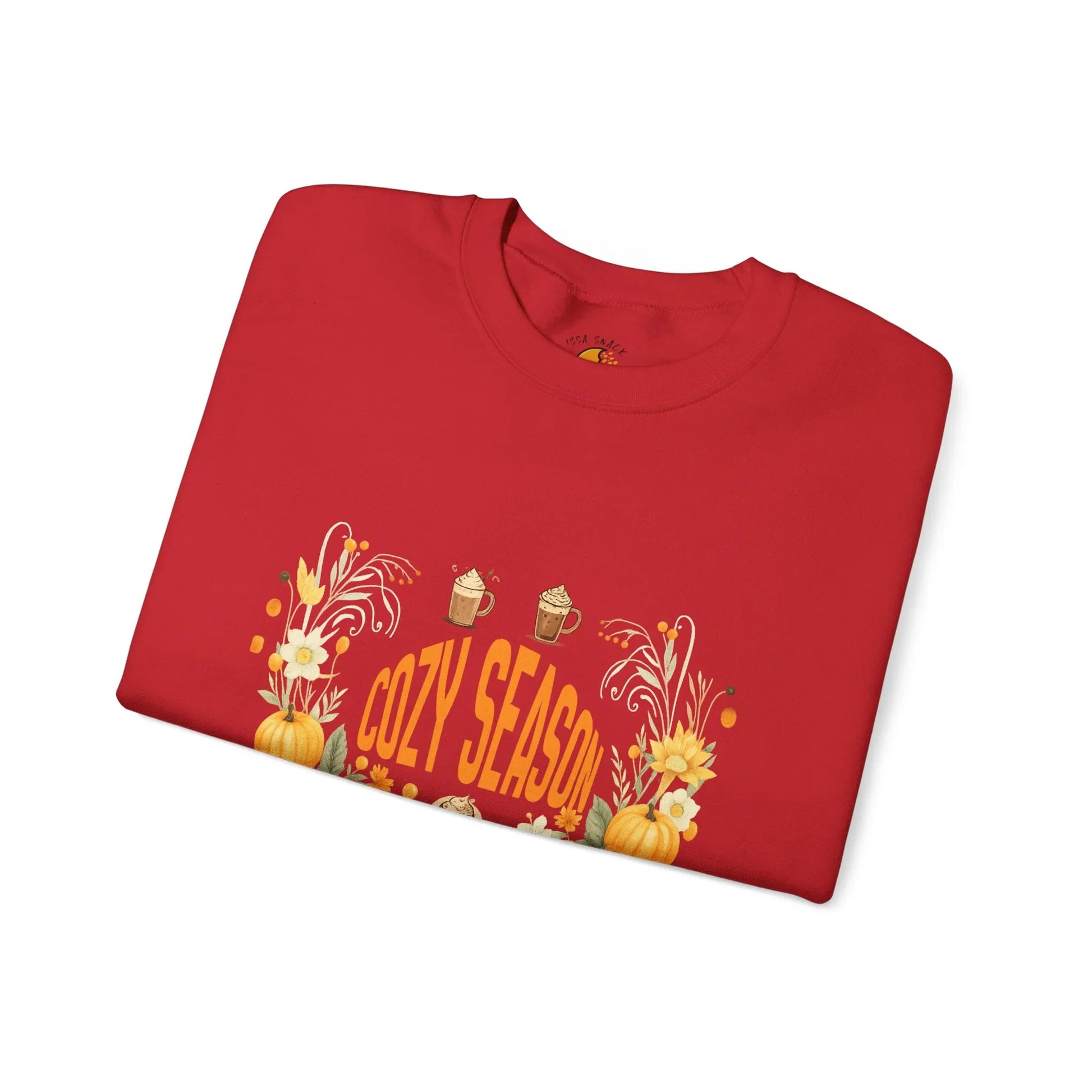 Red folded sweatshirt with Cozy Season text, pumpkins, flowers, and mugs graphic design
