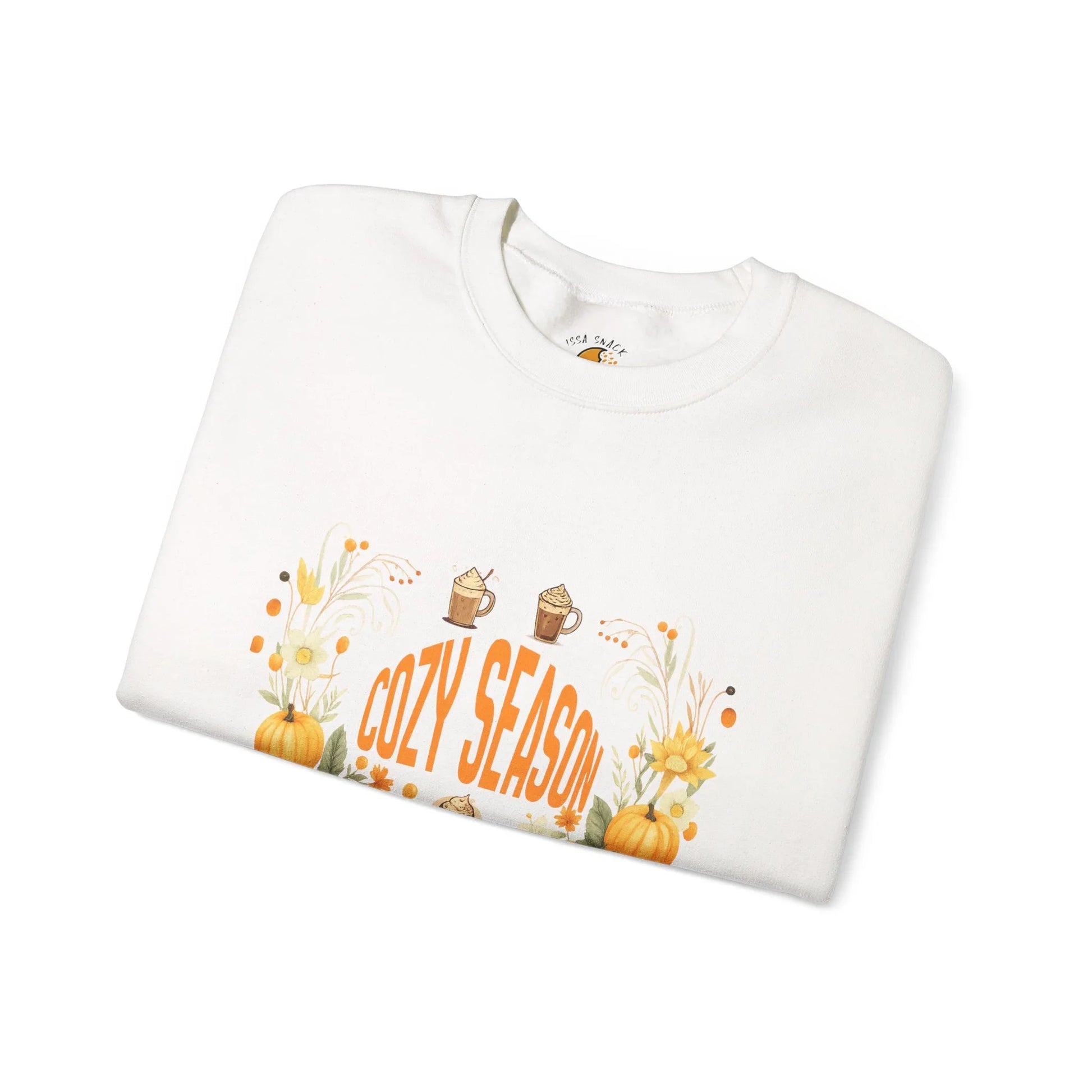 Folded white sweatshirt with 'Cozy Season' text, pumpkins, sunflowers, fall mugs design