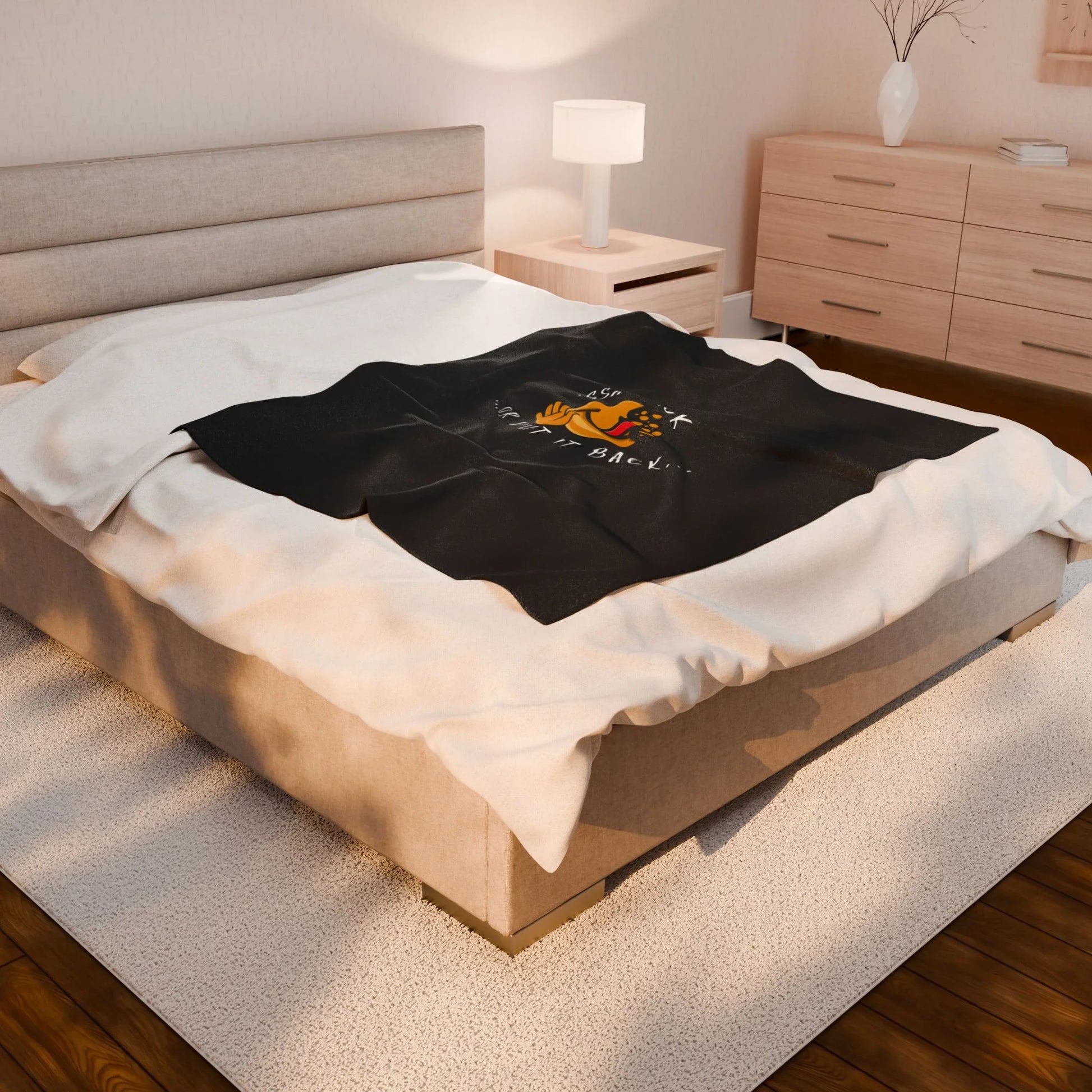Cozy bedroom with beige bed, black throw blanket featuring cartoon dog and text, modern decor