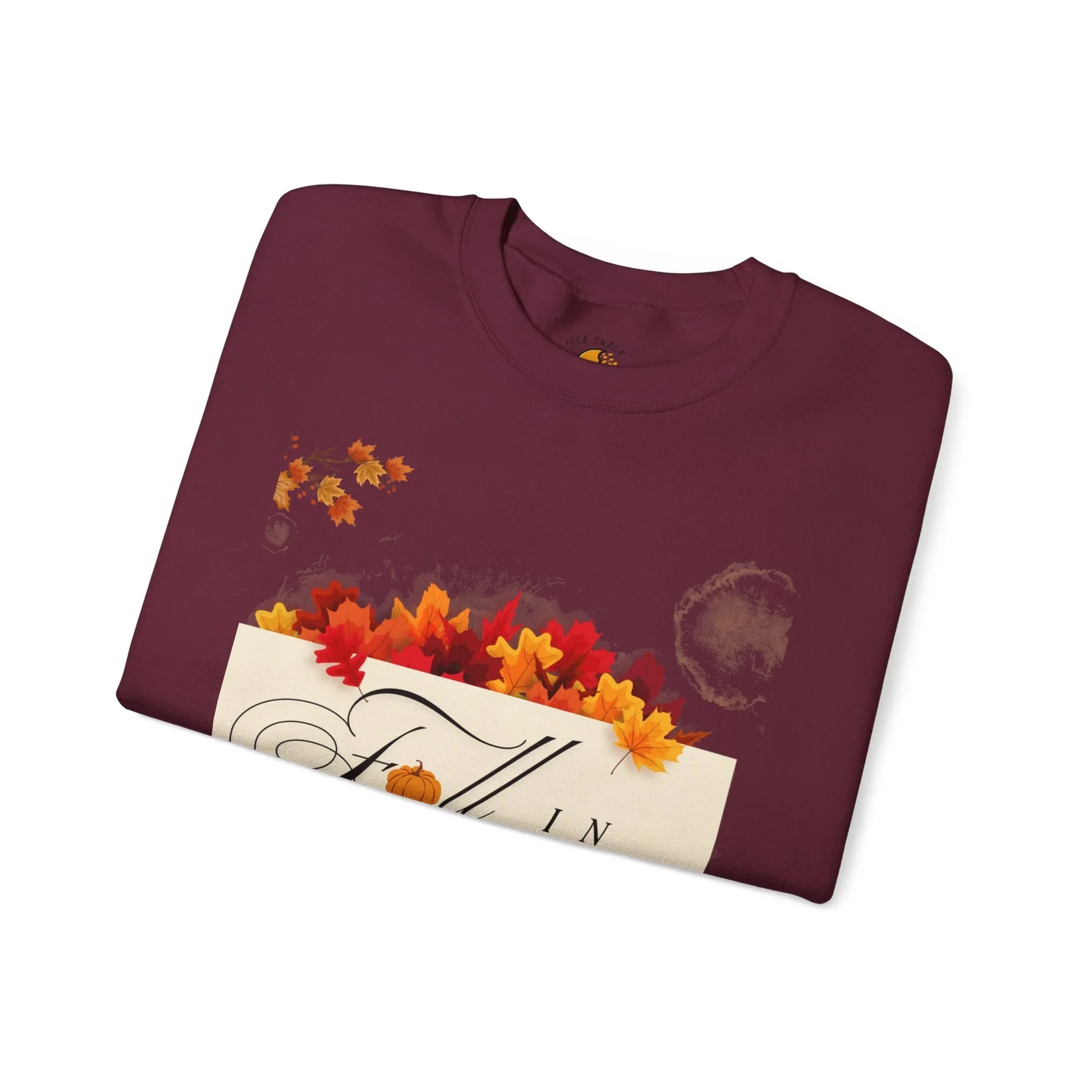 Folded maroon sweatshirt with fall leaves and autumn-themed text design