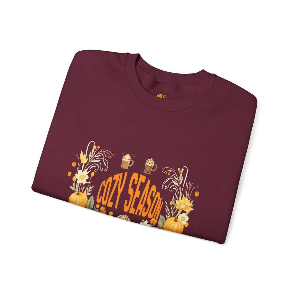 Folded maroon sweatshirt with Cozy Season text, pumpkins, sunflowers, and fall drinks design